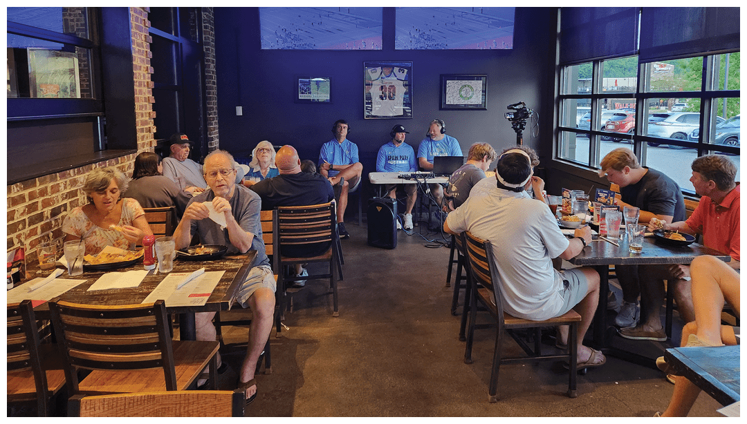 People are sitting at tables in a casual restaurant setting, eating and conversing with each other. Description generated by AI