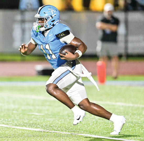 A person wearing a light blue football uniform and helmet is running on a field while holding a football. Description generated by AI