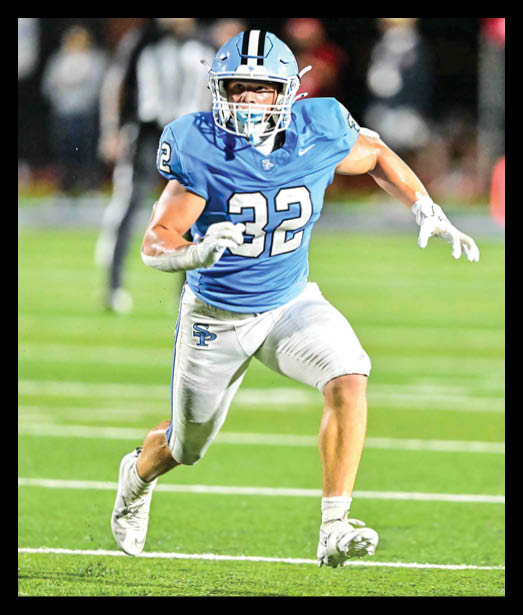 A person wearing a blue football uniform with the number 32 is running on a green field during a game. Description generated by AI
