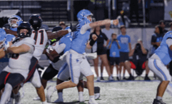 A group of people in football uniforms are actively engaged in a game on a field, with one person in a light blue uniform preparing to throw a football. Description generated by AI