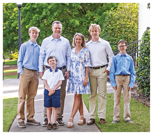 Five people stand on grass and dirt with only their legs and feet visible, wearing casual pants, shorts, and sandals or shoes. Description generated by AI