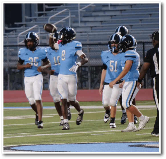 Four people in blue and white football uniforms are standing and walking on a football field near the end zone. Description generated by AI