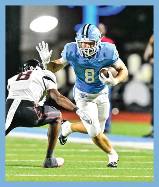 A person in a light blue football uniform with the number 8 is running with the ball while another person in a white and black uniform attempts to block them on a football field. Description generated by AI