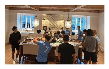 Three people are standing and interacting in a room with wooden walls and a window letting in natural light. Description generated by AI