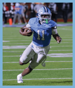 A person wearing a blue football jersey with the number 11 and a helmet is running on a football field while holding a football. Description generated by AI