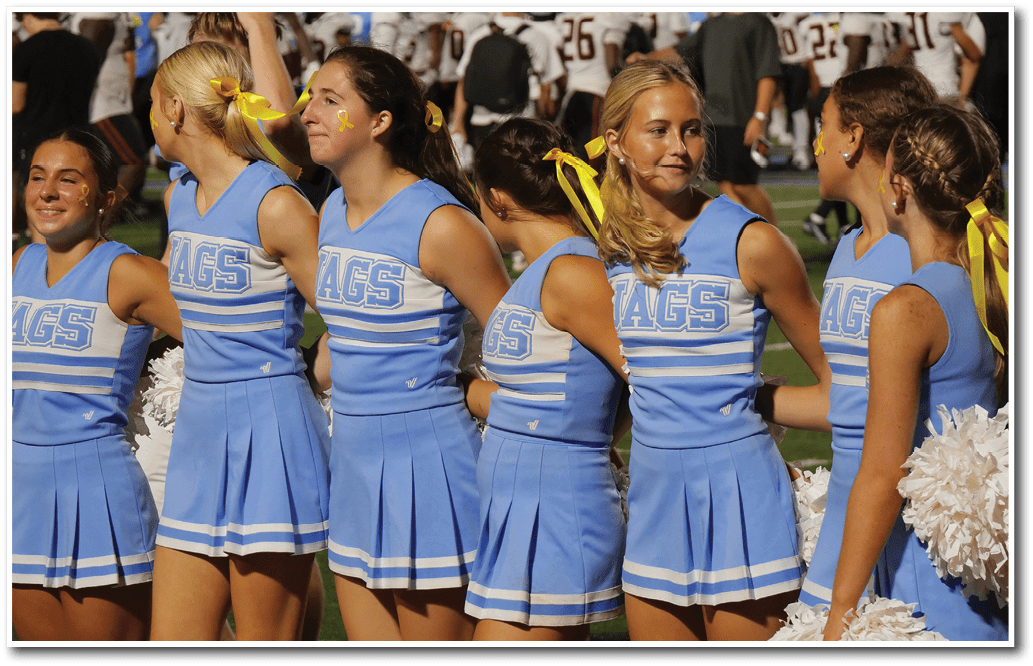 A group of people wearing blue cheerleading uniforms with yellow ribbons in their hair stand closely together on a sports field. Description generated by AI