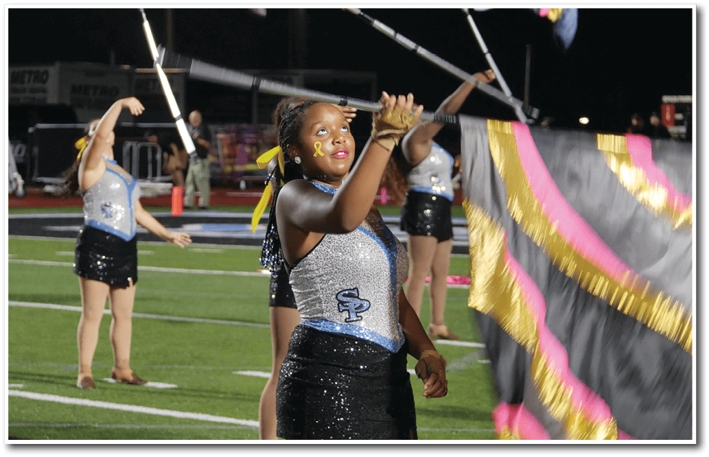 Adults in sparkly performance outfits are twirling flags on a sports field at night. Description generated by AI