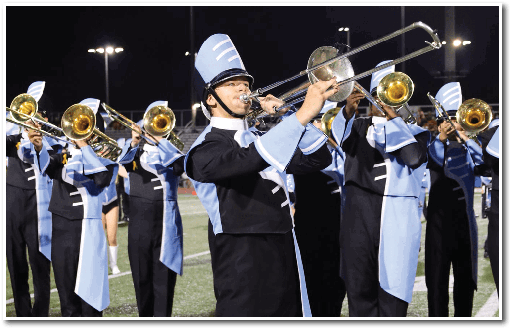 Adults in matching band uniforms are playing trombones outdoors at night under stadium lights. Description generated by AI