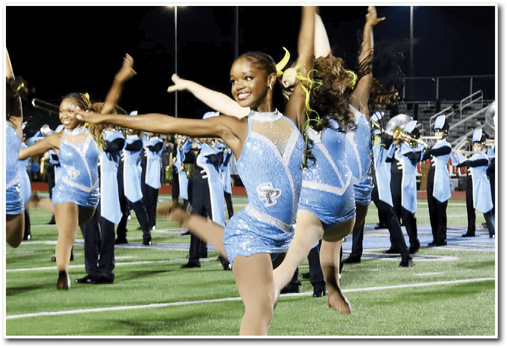 People in sparkling blue costumes are performing a coordinated dance routine outdoors at night under bright stadium lights. Description generated by AI