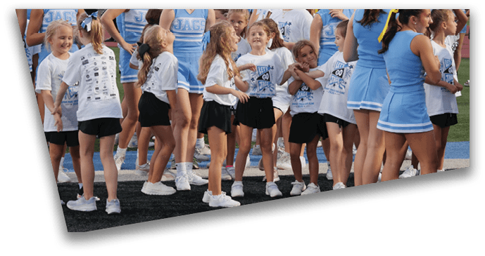 A group of children and adults in cheerleading uniforms and casual sportswear are gathered on a sports field, some smiling and interacting with each other. Description generated by AI