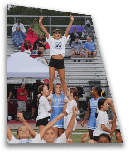 Children and adults in cheerleading uniforms are performing on a sports field with a crowd in the background. Description generated by AI