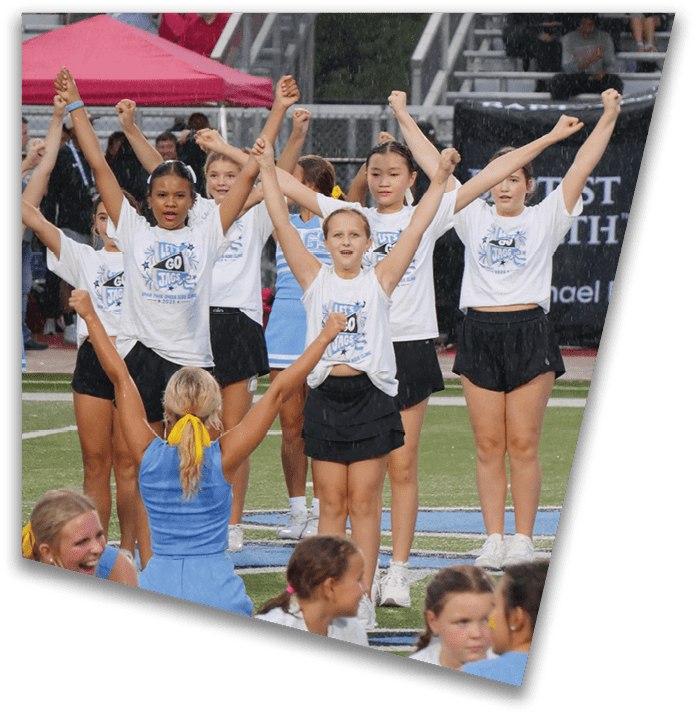 Children and adults in sports attire are gathered on a field, with some standing and others sitting or kneeling, engaged in conversation or activity. Description generated by AI