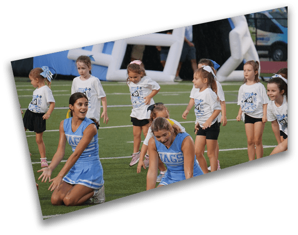 Children and adults in cheerleading uniforms are performing on a sports field with an inflatable structure and a vehicle in the background. Description generated by AI