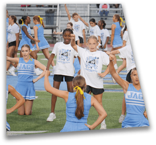 Children in sports uniforms and matching t-shirts are performing a cheerleading routine on a field. Description generated by AI