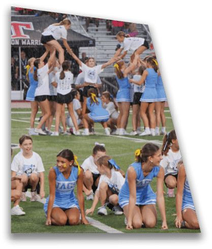 People in cheerleading uniforms are performing stunts and sitting on a sports field during what appears to be a cheerleading practice or event. Description generated by AI