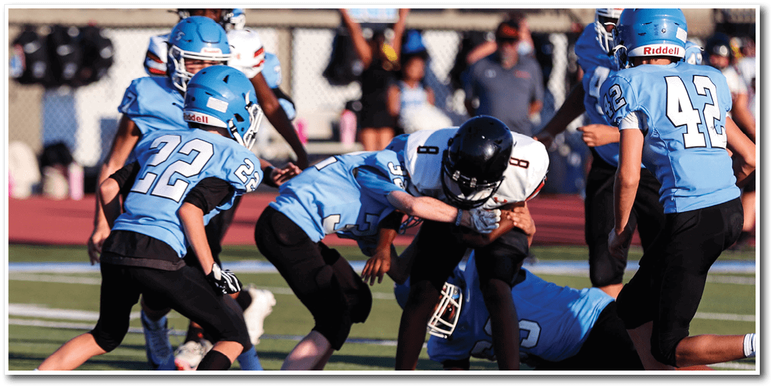 Several people wearing blue football uniforms are tackling a person in a white football uniform on a field. Description generated by AI
