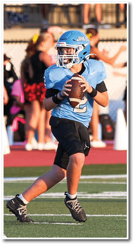 A person wearing a blue football helmet and jersey with the number two is holding a football in a ready-to-throw position. Description generated by AI