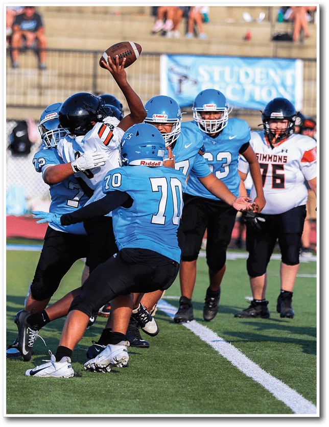 People wearing blue football uniforms and helmets are engaged in a play with one person holding a football ready to throw. Description generated by AI