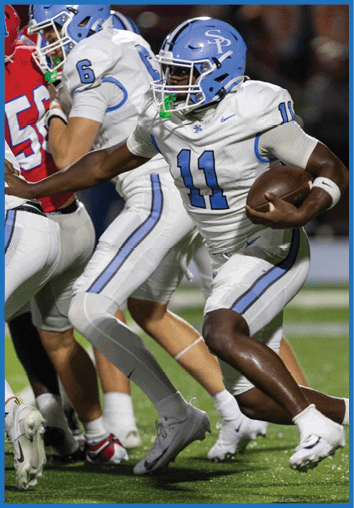 A person wearing a white and blue football uniform with the number 11 is running with a football during a game. Description generated by AI