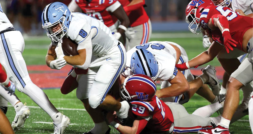 A group of people in football uniforms are engaged in a tackle on a grassy field during a game. Description generated by AI