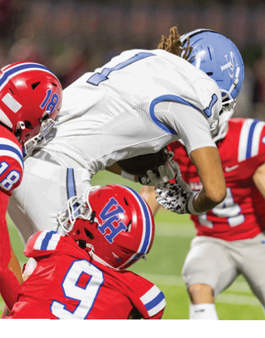 Two people in red football uniforms are positioned on the field facing a person in a white football uniform holding a football. Description generated by AI