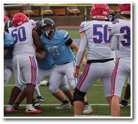 People wearing football uniforms are engaged in a play on a field with school buses visible in the background. Description generated by AI