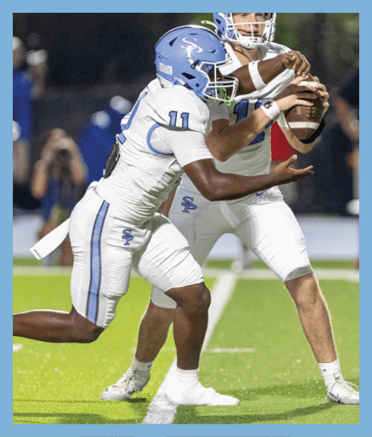 Two people in white and blue football uniforms are on a field with one handing off a football to the other. Description generated by AI