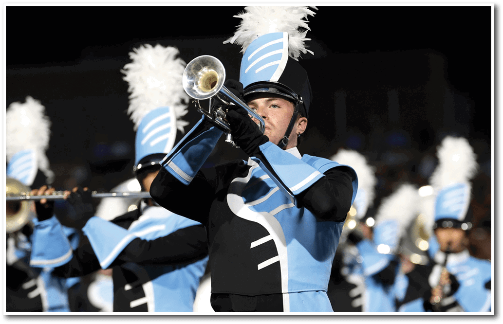 A person in a blue and black marching band uniform is playing a trumpet with other similarly dressed band members in the background. Description generated by AI