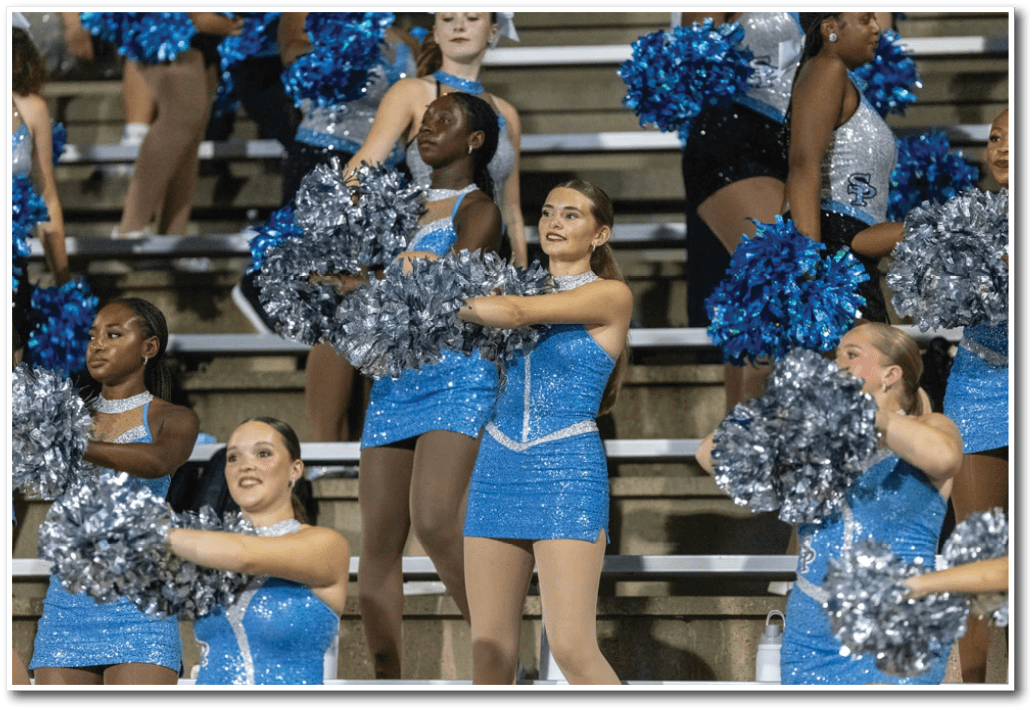 Adults in sparkly blue cheerleading outfits perform a routine with silver and blue pom-poms on bleachers. Description generated by AI