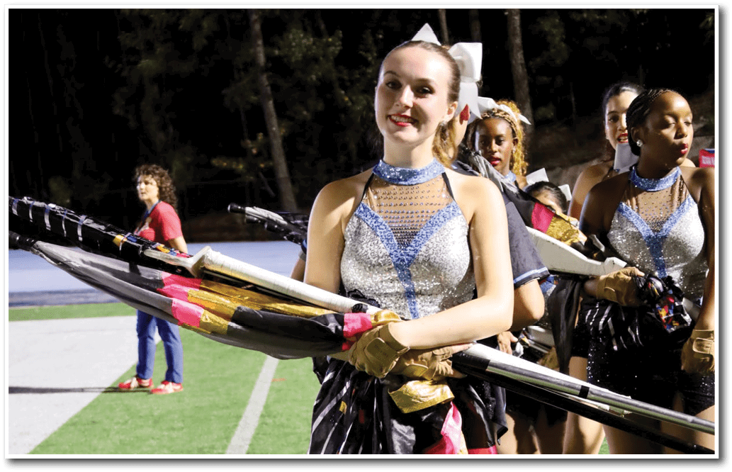 People in sparkling blue and silver performance costumes hold folded flags on a sports field at night. Description generated by AI