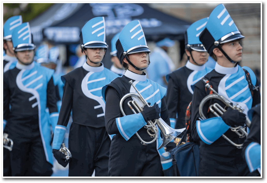 People in matching blue and black marching band uniforms are holding brass instruments while standing in formation. Description generated by AI