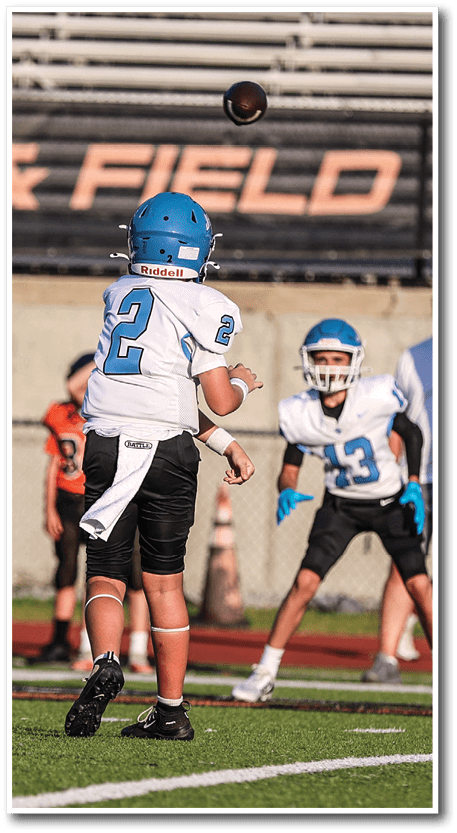 Two people wearing blue helmets and white sports uniforms are playing football, with one person throwing the ball. Description generated by AI