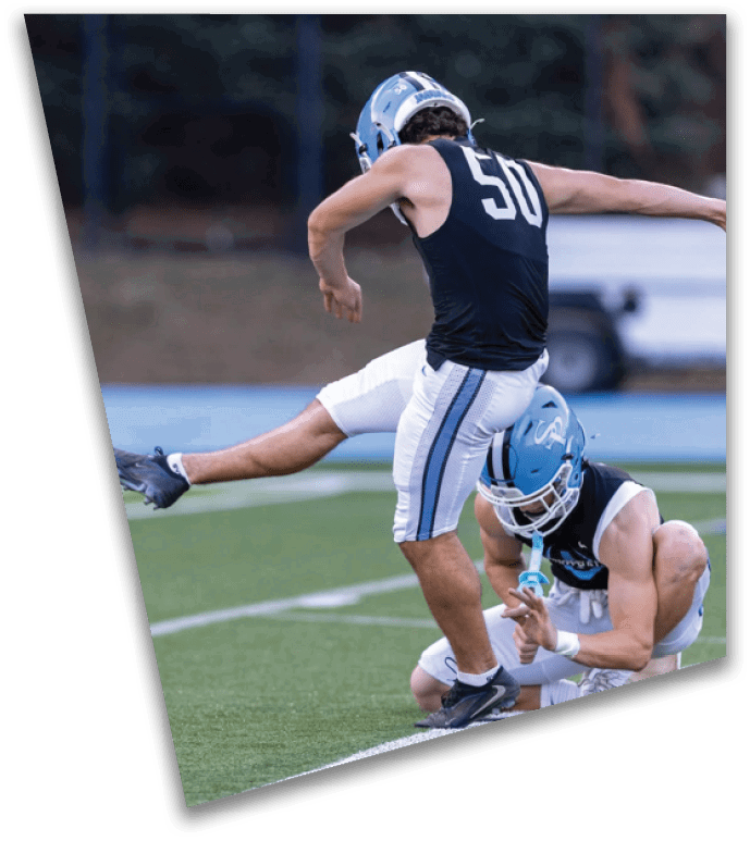 A person wearing a football uniform with the number 56 is kicking a football held by another person kneeling on a grassy field. Description generated by AI