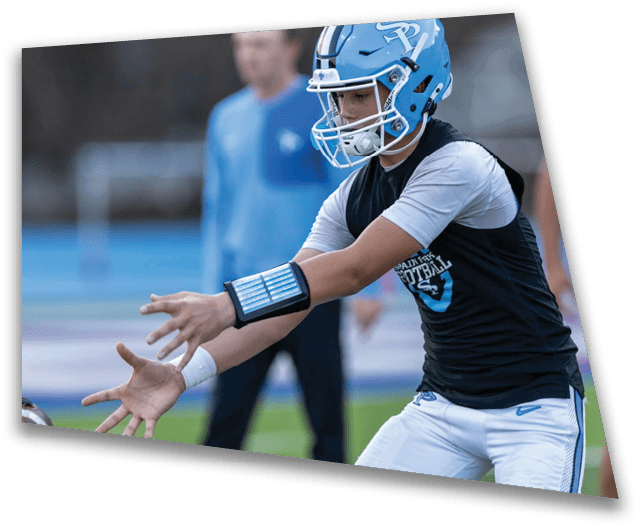A person wearing a black shirt and white pants is reaching out with both hands to catch a football on a sports field. Description generated by AI
