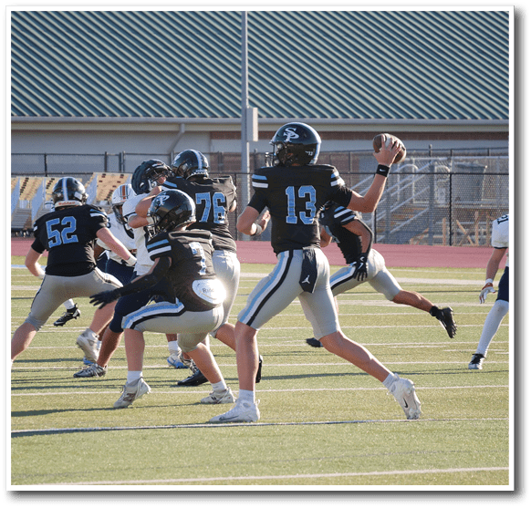 A group of people wearing black and blue football uniforms are on a field with one person preparing to throw a football. Description generated by AI