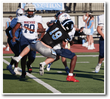 A group of people playing football on a field with one person in a black uniform being tackled by a person in a white uniform while others in white uniforms watch nearby. Description generated by AI