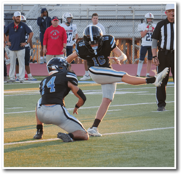 A person wearing a sports uniform is kicking a football on a field while another person stands nearby. Description generated by AI