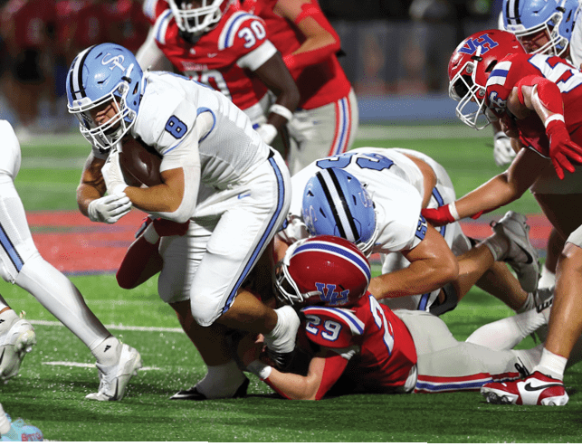 A group of people wearing football uniforms are engaged in a tackle on a grassy field during a game. Description generated by AI