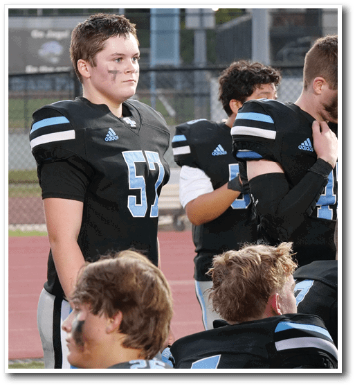 A group of people wearing black and blue football uniforms stand and sit on a sports field with a track in the background. Description generated by AI