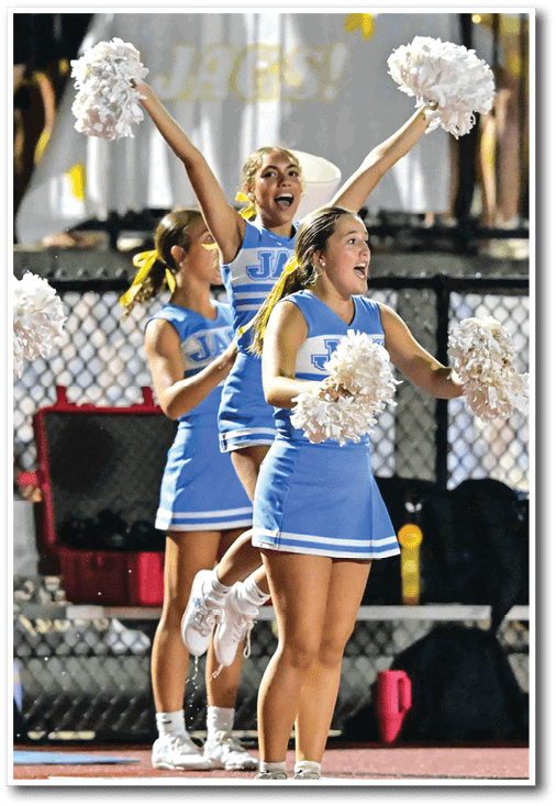 Adults in blue cheerleading uniforms are performing with white pom-poms on a sports field at night. Description generated by AI