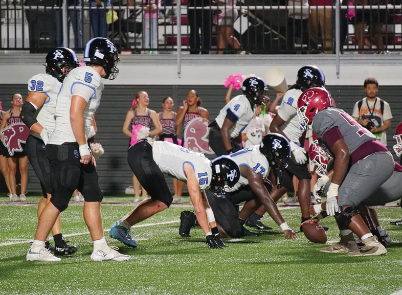 People in football uniforms are lined up on a field facing each other with cheerleaders and spectators in the background. Description generated by AI