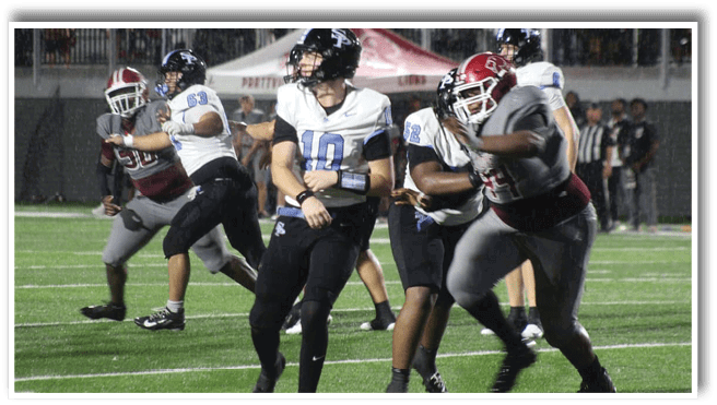 People wearing football uniforms are actively engaged in a game on a grassy field under stadium lights. Description generated by AI