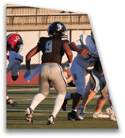 Adults in football uniforms are engaged in a game on a field with bleachers and spectators in the background. Description generated by AI