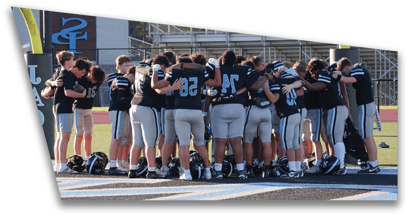 A group of people wearing sports uniforms stand closely together on a field, appearing to be in a team huddle. Description generated by AI