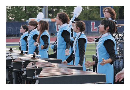 People in blue and black uniforms stand in a row playing percussion instruments on a field, appearing focused and engaged. Description generated by AI