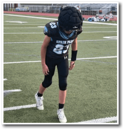A person wearing a black football uniform and helmet is walking on a football field with white yard lines. Description generated by AI