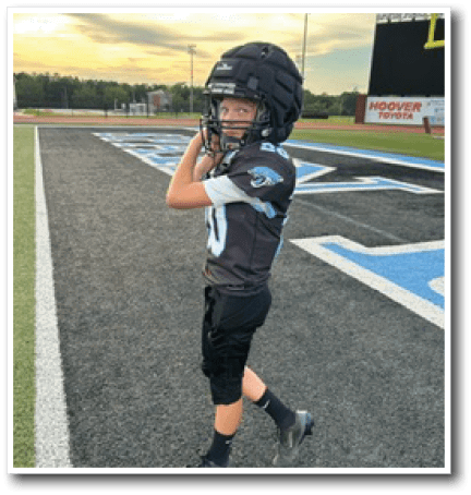A person wearing a football uniform and helmet is standing on a sports field near the end zone at sunset. Description generated by AI