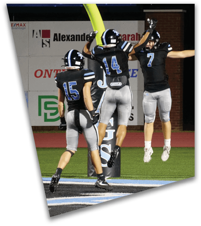 Three people in football uniforms are celebrating on a field near the end zone with one person jumping and two others raising their arms. Description generated by AI