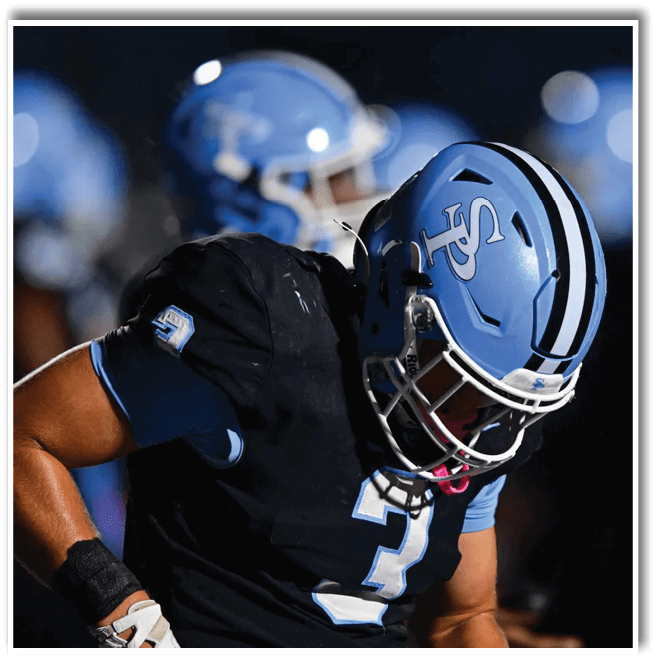 A person wearing a blue helmet and black football uniform with the number three is bent forward in a sports setting. Description generated by AI