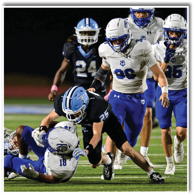 Several people in football uniforms are engaged in a dynamic play on a field, with one person on the ground holding the ball while others attempt to tackle or assist. Description generated by AI